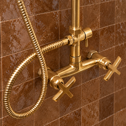 Close-up of Nashville’s unlacquered brass mixer, cross handles, diverter and flexible shower hose against brown tiles