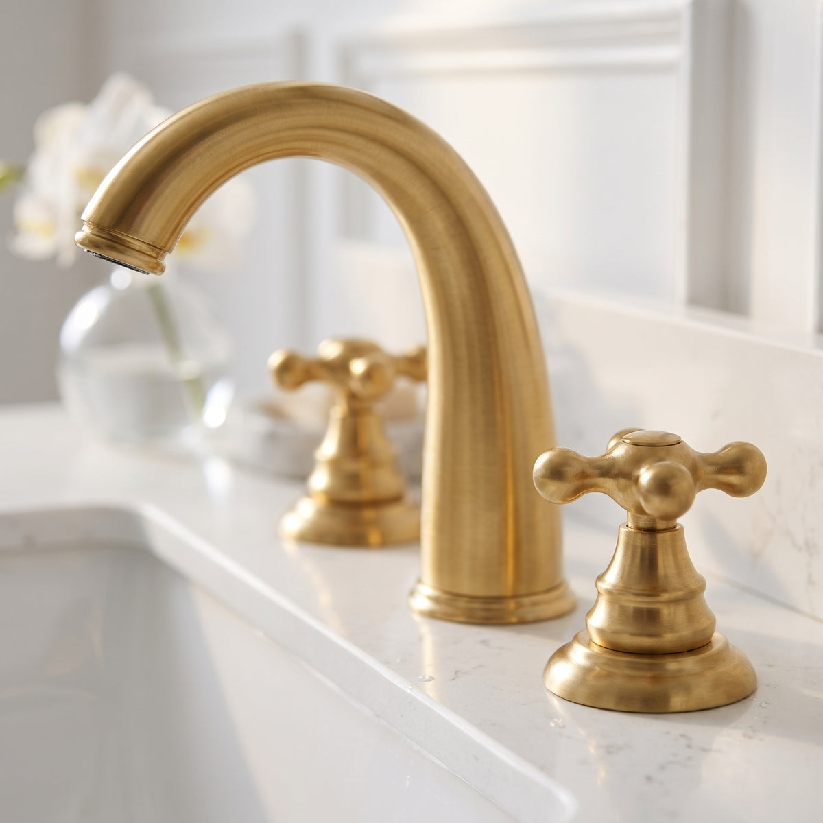 Angled close-up of the unlacquered brass bathroom faucet with cross handles on a white countertop