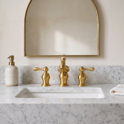 Front view of the traditional widespread bathroom faucet with lever handles on a white vanity beneath an arched mirror