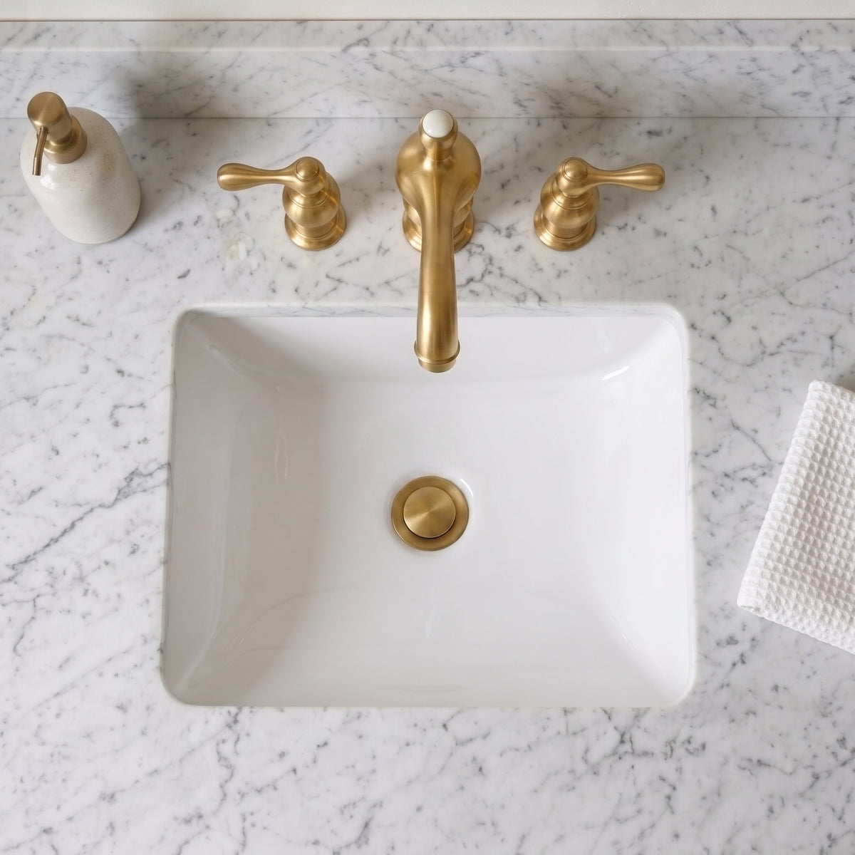 Overhead view of the unlacquered brass bathroom faucet above a rectangular white basin with matching pop-up drain