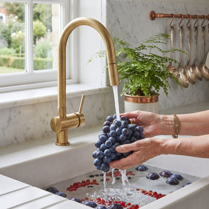 Brewster brass kitchen faucet running water over grapes in a white sink