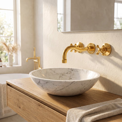 Unlacquered brass bathroom faucet with curved spout above a white veined vessel basin on a wooden vanity beneath a mirror