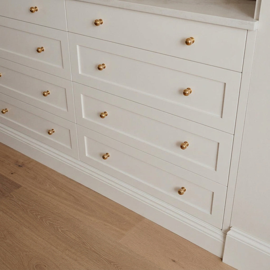 Polished unlacquered brass ball knobs on three wide white Shaker-style drawers beneath a pale countertop