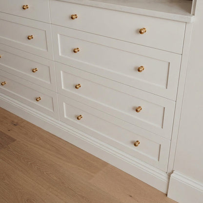 Polished unlacquered brass ball knobs on three wide white Shaker-style drawers beneath a pale countertop